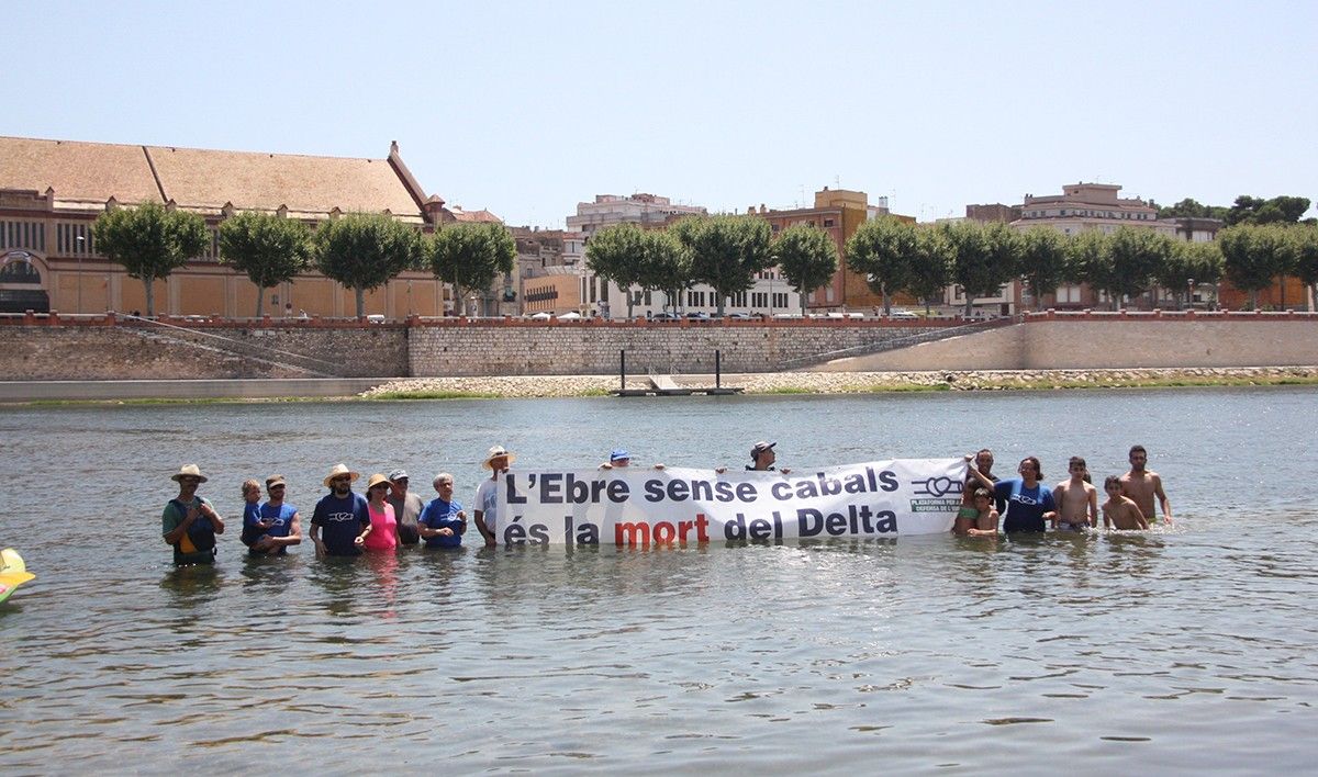 Uns quants participants de la piraguada a l'Ebre mostren dins de l'aigua una pancarta on s'hi llegeix 